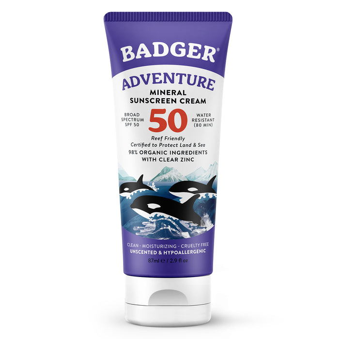 A tube of Badger Adventure Mineral Sunscreen Cream SPF 50, featuring orca illustrations and mountains on the label. The tube highlights broad spectrum protection, water resistance, and organic ingredients.