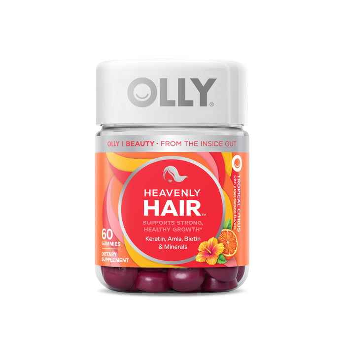 A bottle of OLLY Heavenly Hair gummies with a white cap, bright pink and orange label, and images of tropical fruits. The label states it supports strong, healthy hair growth and contains keratin, amla, biotin, and minerals.