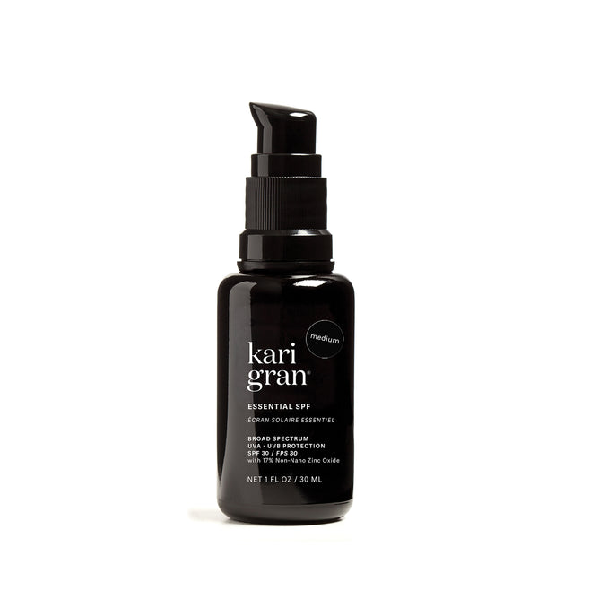 A black pump bottle of Kari Gran Essential SPF sunscreen, labeled as medium shade and broad spectrum UVA/UVB protection, standing upright on a white background.