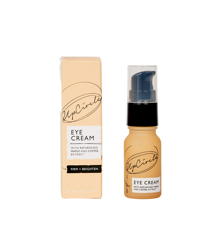 A bottle of UpCircle Eye Cream with repurposed maple and coffee extract is shown next to its beige box packaging on a white background. The bottle has a black pump and both items display the UpCircle logo.