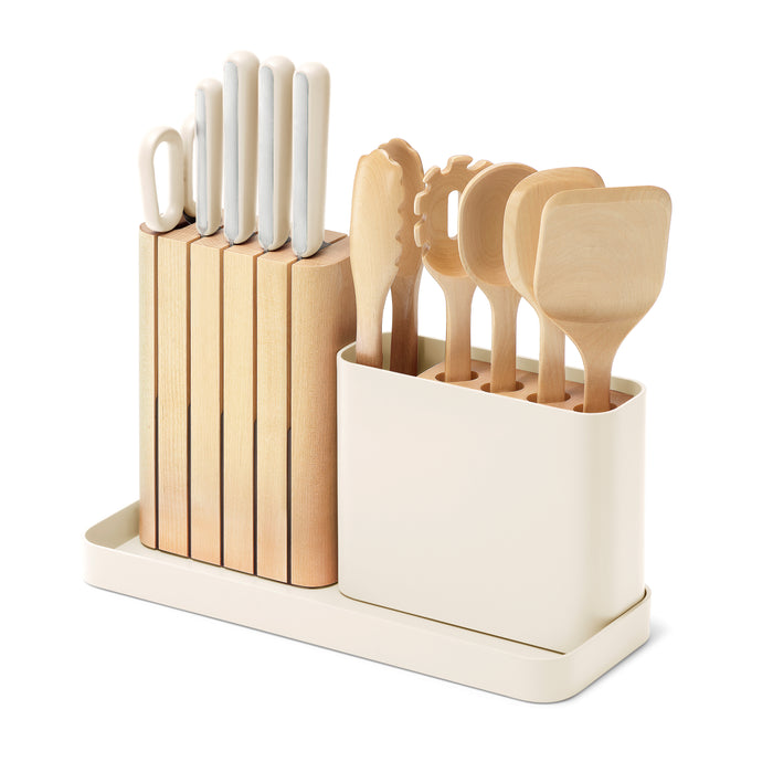 A cream-colored kitchen utensil holder containing six knives with white handles and six wooden cooking utensils, including spatulas, a spoon, and a pasta server, all organized neatly.