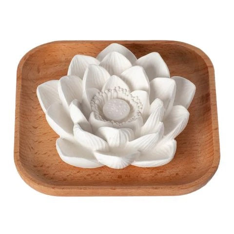A white ceramic lotus flower ornament sits on a square wooden tray, viewed from above.