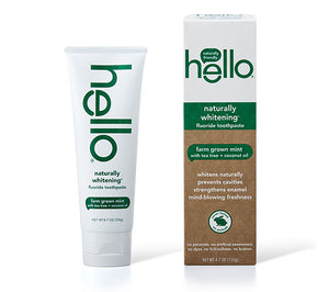 Hello Naturally Whitening Fluoride Toothpaste comes in tube and box packaging, featuring farm-grown mint, tea tree, and coconut oil. The white and green design highlights its natural ingredients that help prevent cavities and strengthen enamel.