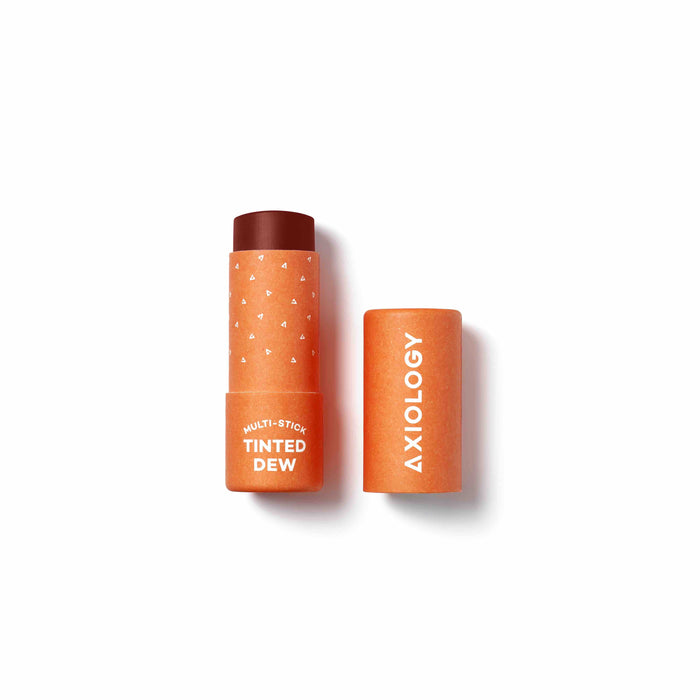 An orange Axiology Multi-Stick Tinted Dew makeup stick with the cap removed and placed next to it, revealing the dark tinted product inside, on a white background.