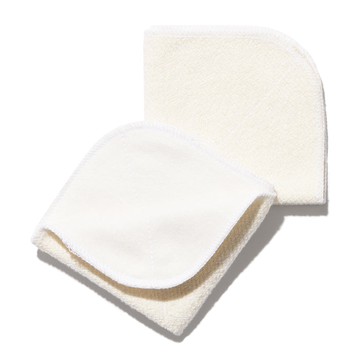 Two off-white, square, reusable fabric pads with rounded corners, slightly overlapping each other on a white background. The pads have visible stitching along the edges.