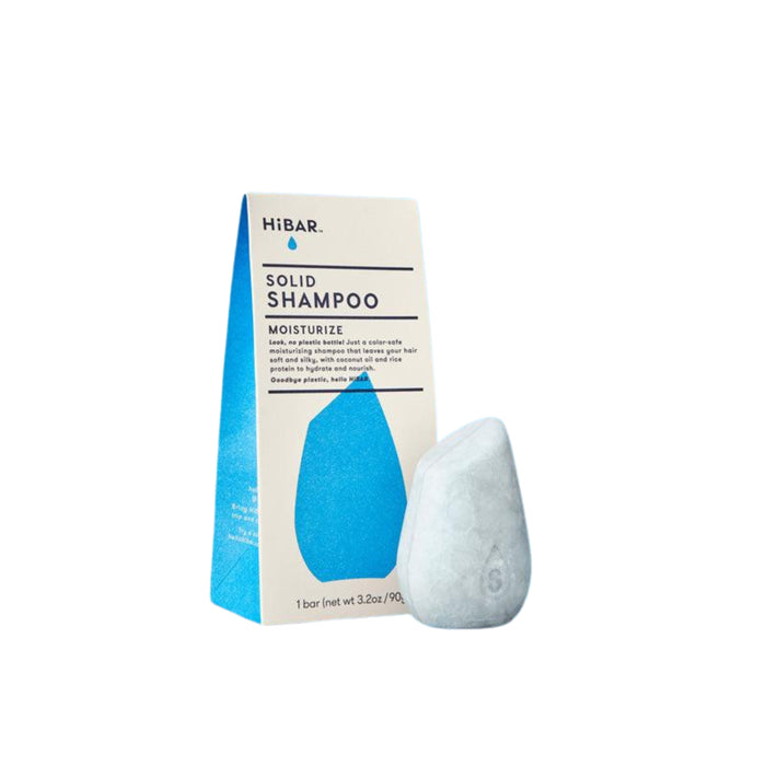 A package of HiBAR Solid Shampoo in blue and cream colors is shown next to a teardrop-shaped, light gray solid shampoo bar. The product is labeled “Moisturize” and weighs 3.2 oz (90 g).