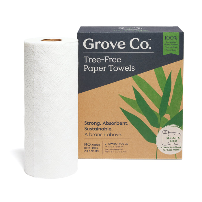 A roll of white paper towels stands beside a box labeled Grove Co. Tree-Free Paper Towels featuring green leaves and eco-friendly claims, including Strong. Absorbent. Sustainable. and 2 Jumbo Rolls.