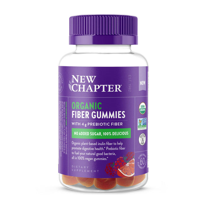 A bottle of New Chapter Organic Fiber Gummies with a purple cap and label, highlighting 4g prebiotic fiber, no added sugar, and organic ingredients. The bottle shows fruit illustrations and contains round, orange gummies inside.