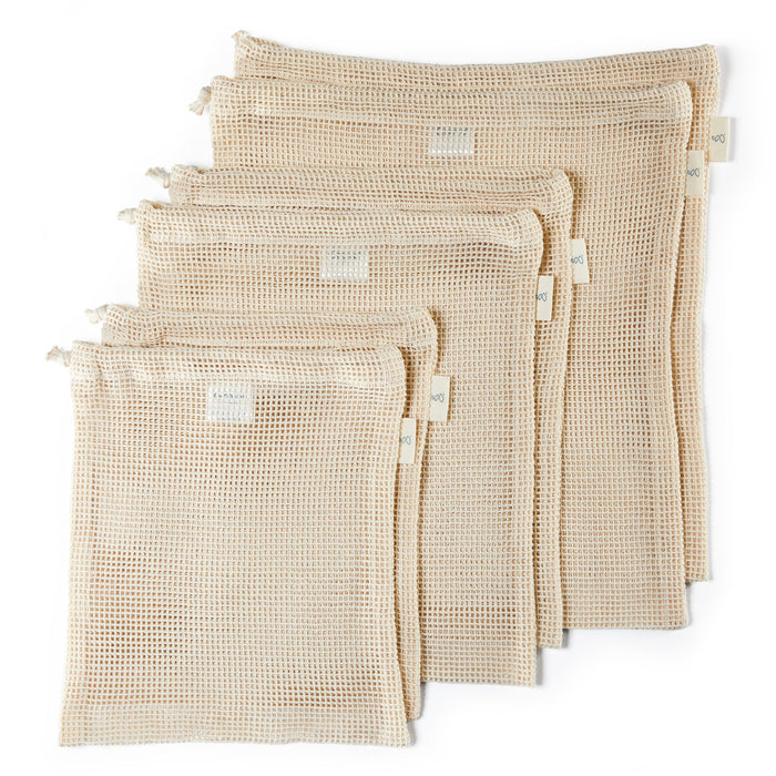 Five beige, reusable mesh produce bags of varying sizes are arranged overlapping each other on a white background, each with a drawstring closure at the top and a small label on the side.