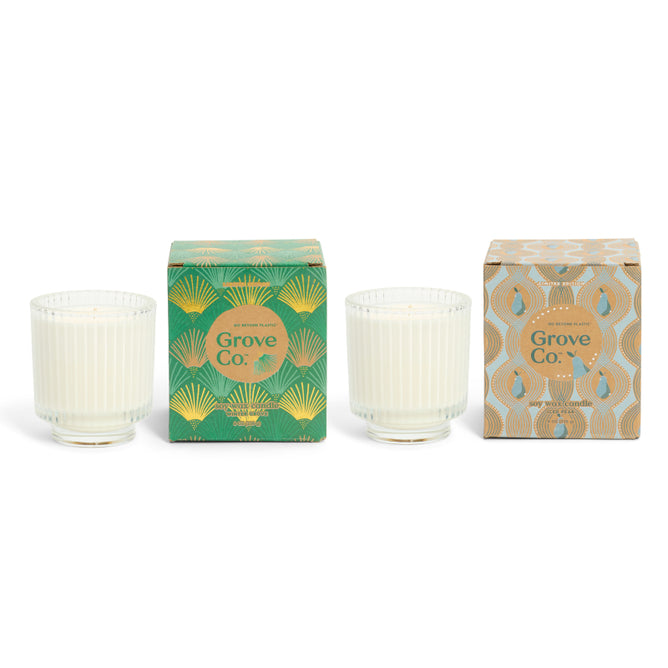 The Grove Co. Winter Glow Set from the Winter Collection features two white soy wax candles in ribbed glass jars and decorative green and gold patterned boxes, beautifully arranged for a festive touch.