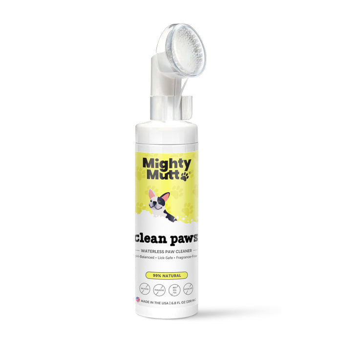 A bottle of Mighty Mutt Clean Paws waterless paw cleaner with a brush attached to the cap, featuring a cartoon dog and yellow label stating it is 99% natural, lick-safe, and fragrance-free.