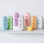 Seven method Body Wash bottles in various colors and scents are arranged on a hexagonal tiled surface. Each bottle highlights plant-based cleansers and a cruelty-free formula. Nearby, a cheerful yellow bath sponge completes the scene.