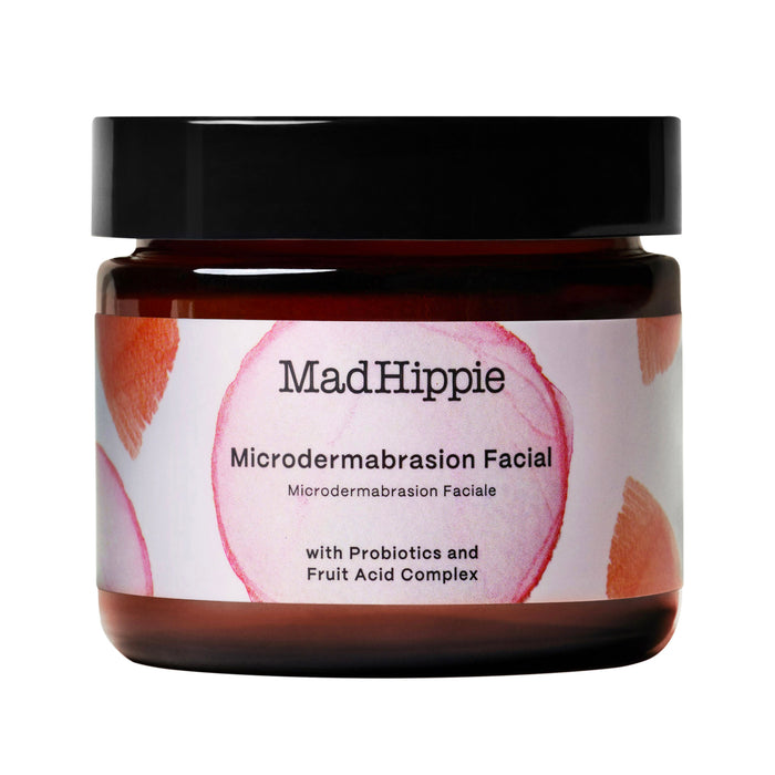 A brown jar with a black lid labeled “Mad Hippie Microdermabrasion Facial,” featuring a pink and orange abstract design. The label mentions probiotics and fruit acid complex as ingredients.
