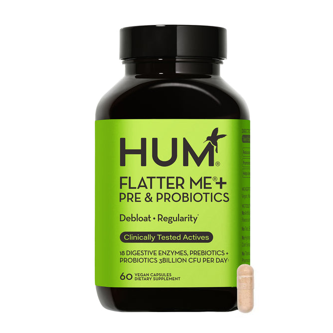 A black bottle of HUM Nutritions Flatter Me - Debloat Enzymes + Pre and Probiotics For Regularity sits alongside a small beige capsule. The green label promotes debloating, regularity, vegan capsules, digestive enzymes, and probiotics to aid digestion.