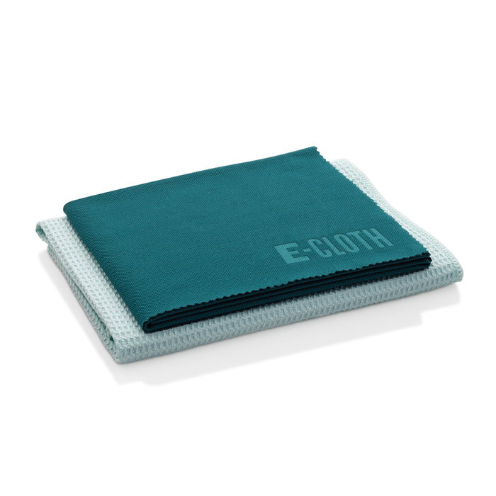 Two neatly folded cleaning cloths are stacked on top of each other; the top cloth is teal with E-CLOTH embossed in the corner, and the bottom cloth is light blue with a textured pattern.