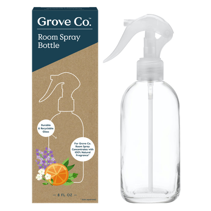 A clear glass spray bottle with a white trigger next to its box, which reads Grove Co. Room Spray Bottle. The box shows an illustration of the bottle and images of flowers and an orange slice.