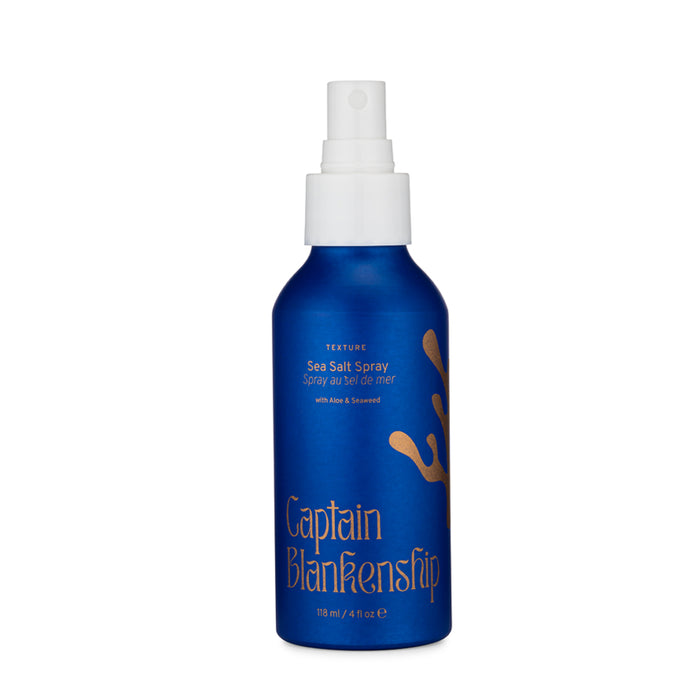 A blue spray bottle labeled Captain Blankenship Sea Salt Spray with gold coral design, white spray nozzle, and text indicating its for texture with aloe and seaweed, 118 ml (4 fl oz).