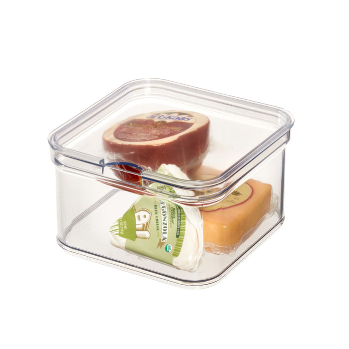 A clear, square plastic container holds three blocks of cheese, each wrapped in different packaging, against a white background.