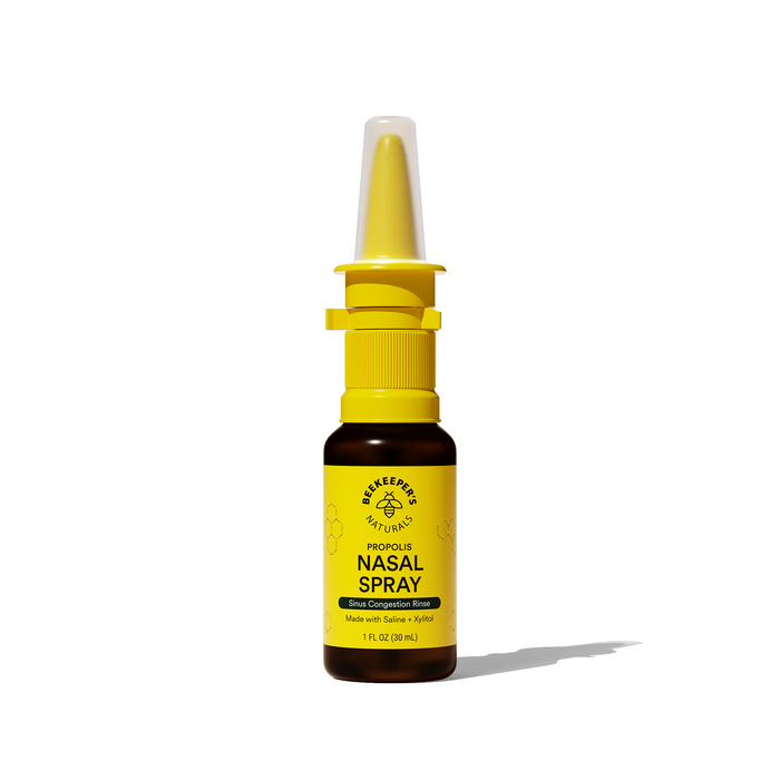 A brown bottle of Beekeeper’s Naturals Propolis Nasal Spray with a yellow cap and nozzle, labeled for sinus congestion relief, sits on a white background casting a shadow.