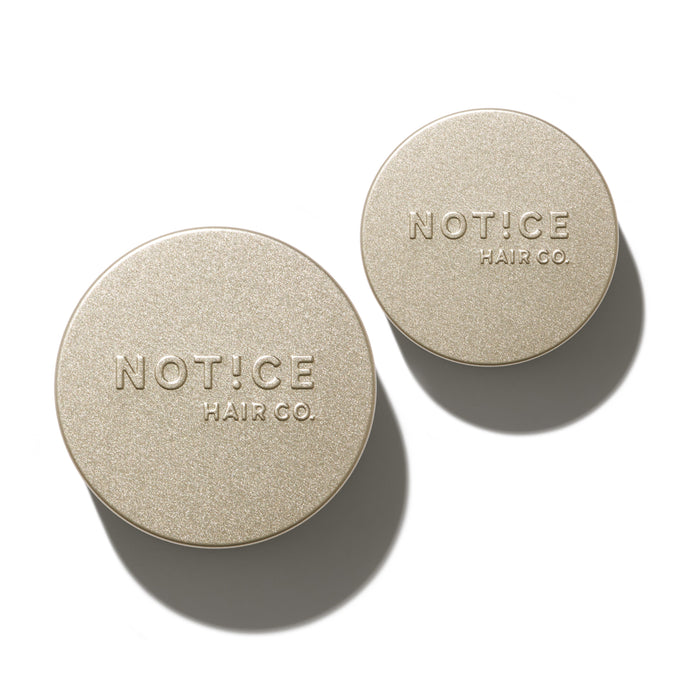 Two round, gold-colored containers with NOTICE HAIR CO. embossed on their lids, casting shadows on a white background. One container is larger than the other.