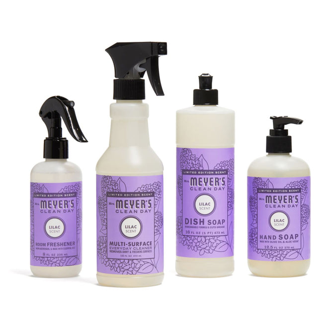 Four bottles of the In Full Bloom Cleaning Set by Grove Collaborative are beautifully displayed. From left to right: room freshener, multi-surface cleaner, dish soap, and hand soap—all with lilac-scented labels featuring floral designs.