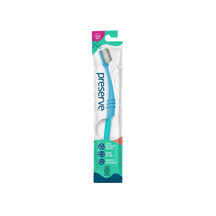 A blue Preserve toothbrush in its original packaging, labeled as ultra soft and made from recycled materials. The packaging highlights eco-friendly features and has a clear window displaying the toothbrush.