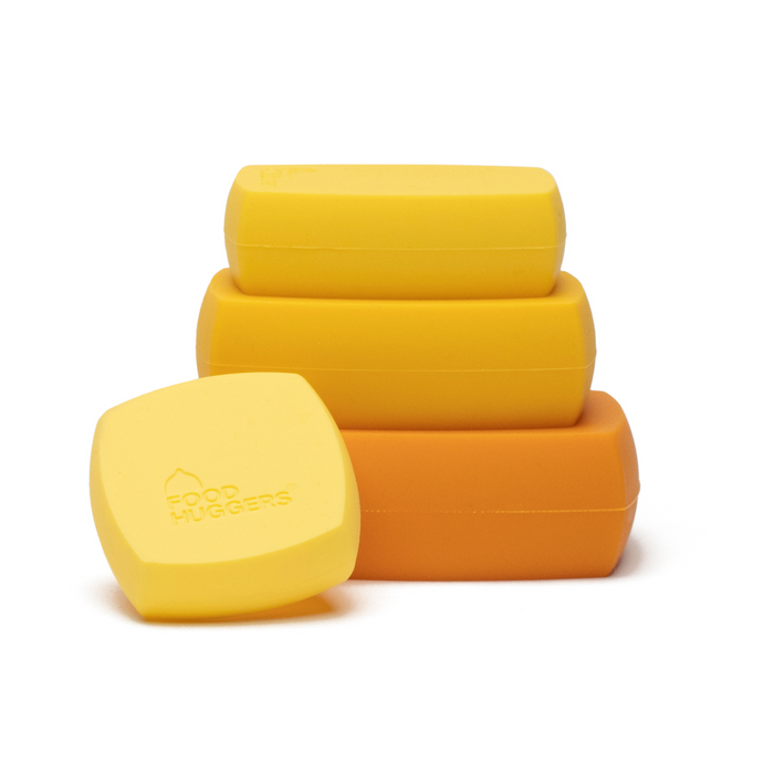 Four stackable, rectangular, bright yellow and orange silicone food savers are shown. The front item is labeled Food Huggers. They are designed to preserve cut produce or unused food.