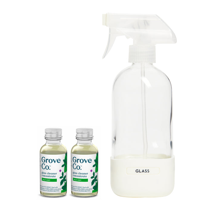 The Glass Cleaner Starter Set by Grove Co. includes a GLASS labeled clear glass spray bottle with a white nozzle and the Slide + Snap labeling system, plus two small bottles of glass cleaner concentrate with green labels and leaf designs for sustainable cleaning.