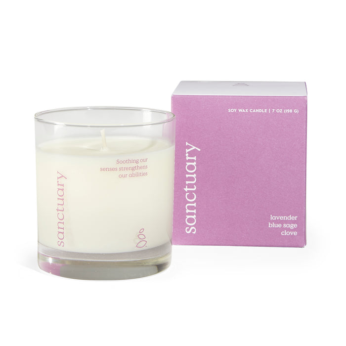 A glass jar candle labeled sanctuary sits next to its lavender-colored box, which reads sanctuary and lavender blue sage clove. The candle label says, Soothing our senses strengthens our abilities.