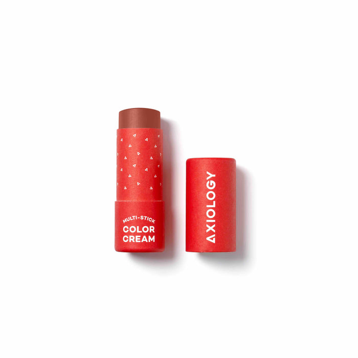 A red tube of Axiology Multi-Stick Color Cream with the cap off and lying next to it, revealing the brownish cream product inside. The tube and cap are labeled in white text.