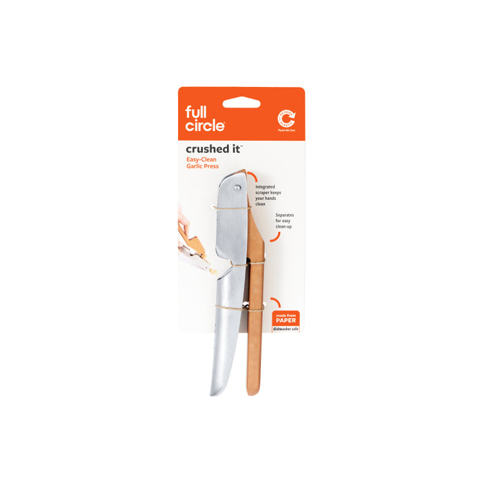 A packaged Full Circle Crushed It Easy-Clean Garlic Press, featuring a silver metal body and a light brown handle, displayed against a white background.