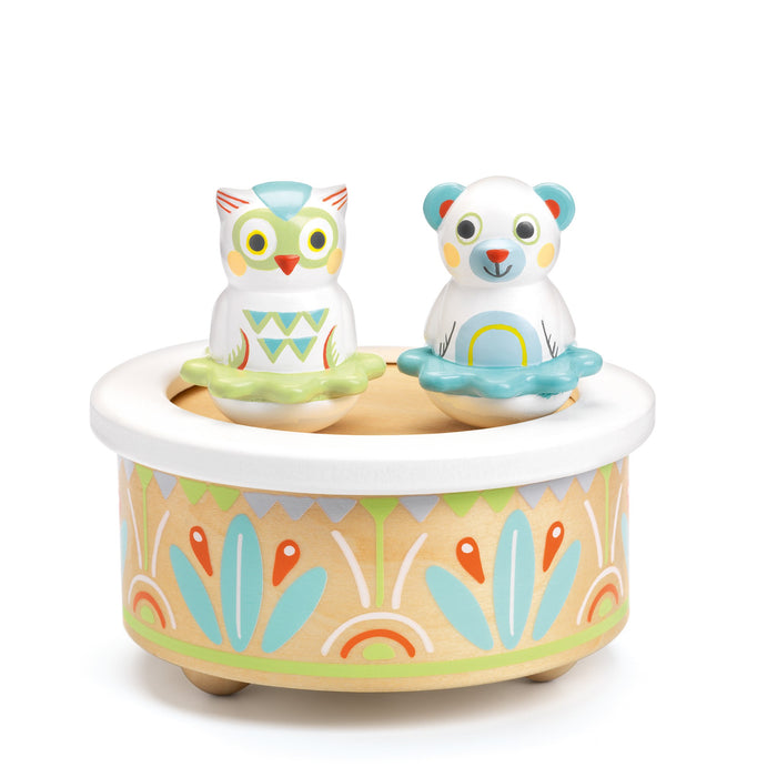 A colorful wooden music box features a painted owl and bear sitting on top, each holding a green ring, with decorative patterns in orange, blue, and green around the base.