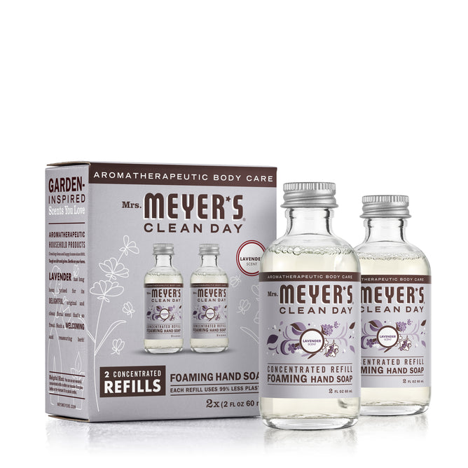 Two clear glass bottles of Mrs. Meyer’s Clean Day foaming hand soap concentrated refills stand next to their packaging box, which features lavender scent details and product imagery.